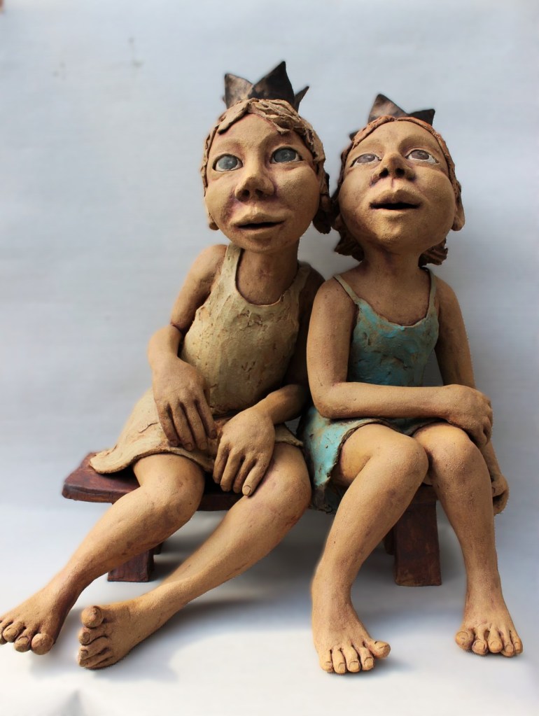 Kleine prinsesjes met kroontje op een bankje. Beeld in keramiek van Kaatje Grauls